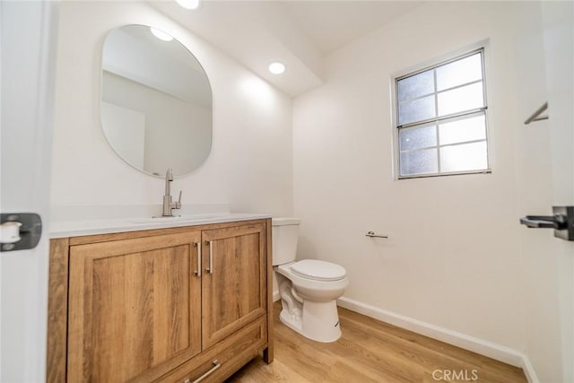 half bath with wood finished floors, vanity, baseboards, toilet, and recessed lighting