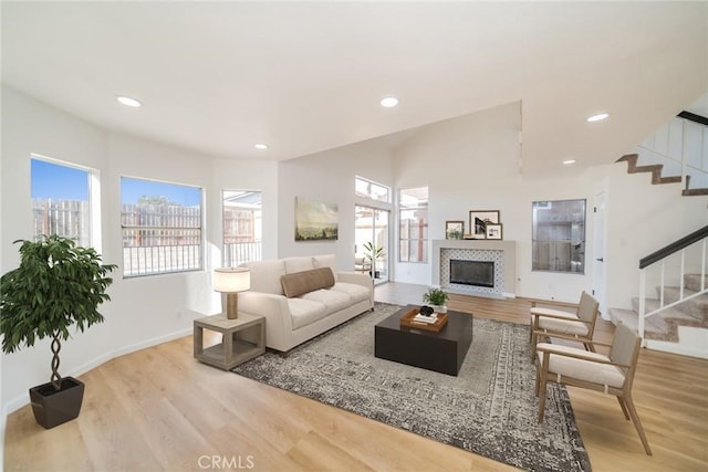 living room with baseboards, stairway, light wood-type flooring, recessed lighting, and a tile fireplace