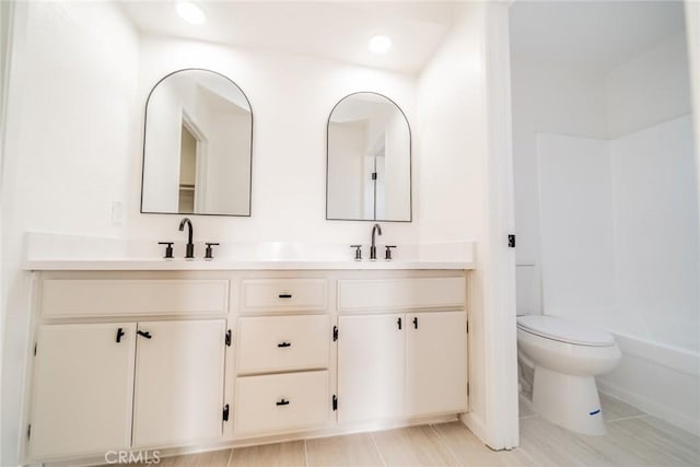 bathroom with baseboards, double vanity, toilet, and a sink
