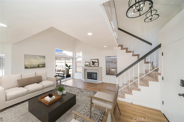living room with a tiled fireplace, stairs, wood finished floors, and a notable chandelier