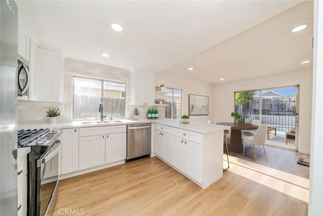 kitchen featuring white cabinets, appliances with stainless steel finishes, light countertops, light wood-style flooring, and a peninsula