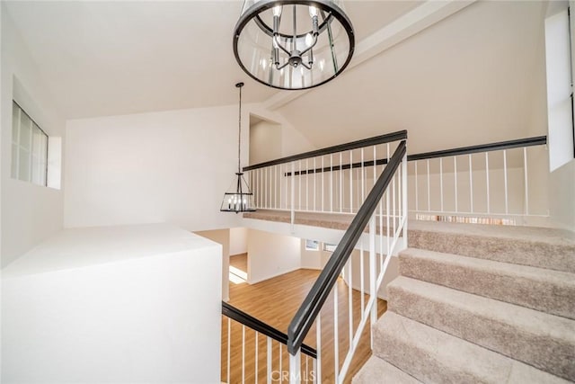staircase featuring vaulted ceiling, wood finished floors, and a chandelier
