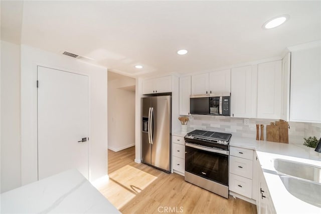 kitchen with appliances with stainless steel finishes, a sink, light wood-style flooring, white cabinetry, and tasteful backsplash