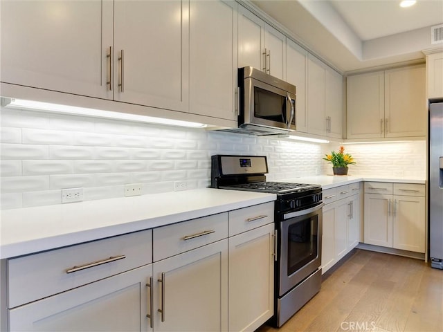 kitchen with decorative backsplash, visible vents, light wood-type flooring, light countertops, and stainless steel appliances
