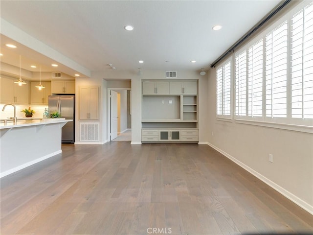 unfurnished living room with visible vents, a sink, baseboards, dark wood-style floors, and recessed lighting