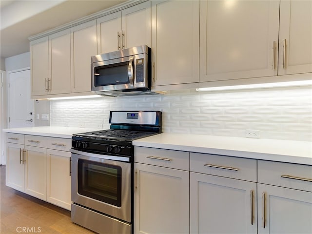 kitchen featuring backsplash, appliances with stainless steel finishes, light countertops, gray cabinetry, and light wood-style floors