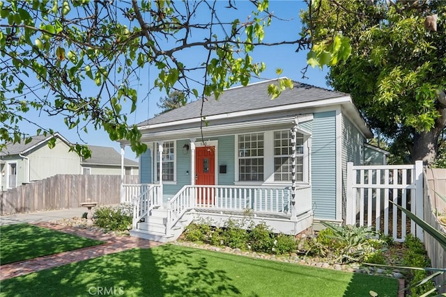 bungalow-style home featuring a porch, fence, a shingled roof, and a front lawn