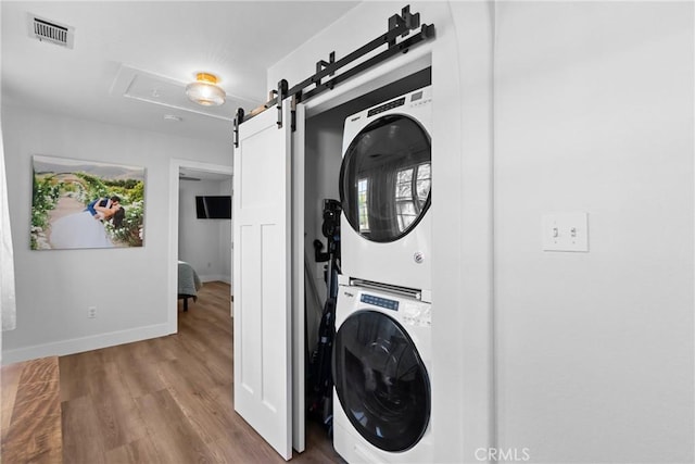 laundry room featuring visible vents, stacked washer and dryer, laundry area, wood finished floors, and a barn door