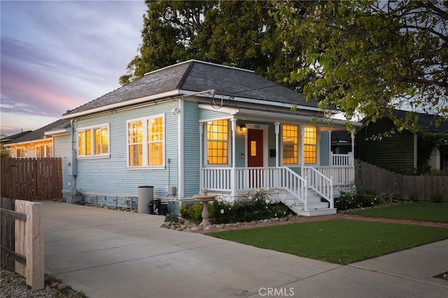 view of front facade featuring covered porch, a lawn, fence, and a shingled roof