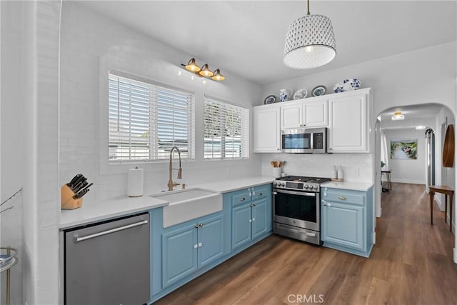 kitchen featuring blue cabinetry, arched walkways, dark wood finished floors, a sink, and stainless steel appliances