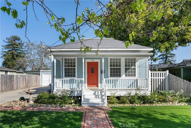 bungalow-style house featuring roof with shingles, fence, covered porch, and a front yard