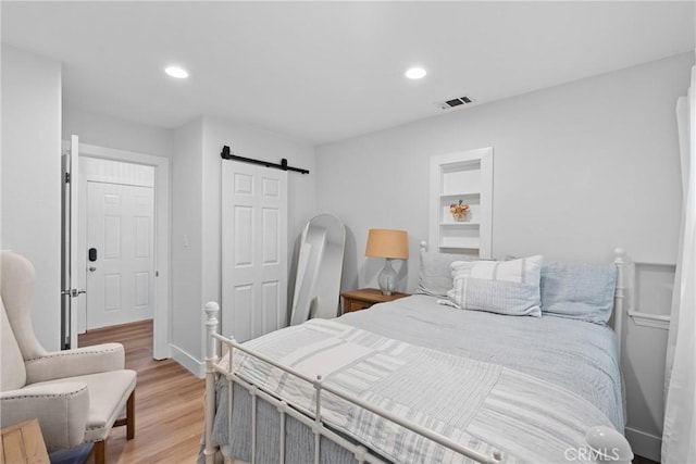 bedroom featuring light wood-style flooring, recessed lighting, a barn door, and visible vents