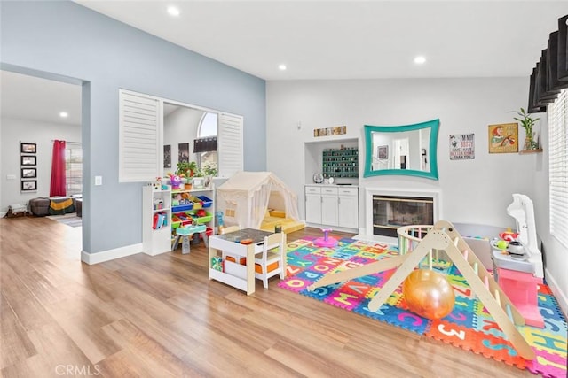recreation room with recessed lighting, baseboards, a glass covered fireplace, and wood finished floors