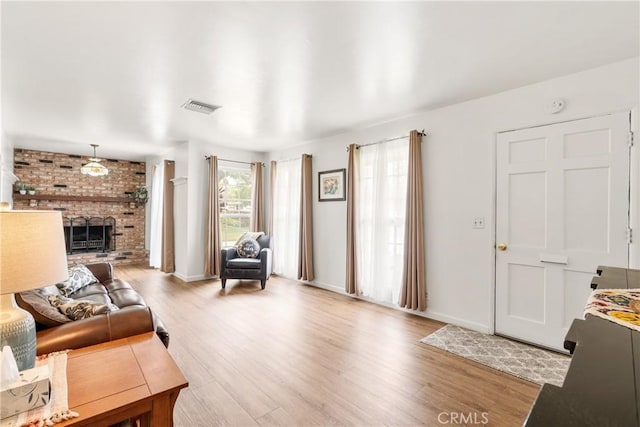 living area featuring visible vents, baseboards, a brick fireplace, and wood finished floors