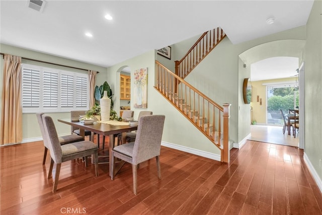 dining area featuring visible vents, arched walkways, stairs, and wood finished floors