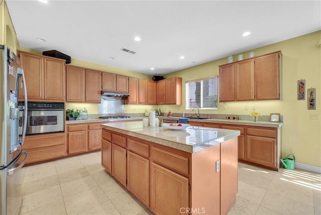 kitchen featuring appliances with stainless steel finishes, a sink, light tile patterned floors, under cabinet range hood, and a kitchen island