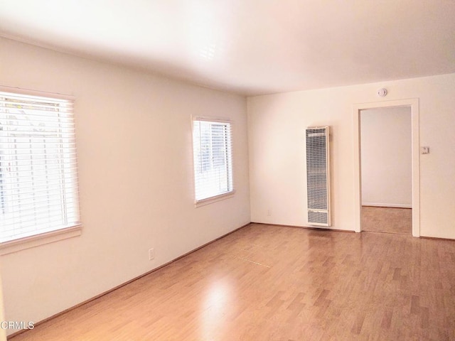 empty room with baseboards, a heating unit, and light wood-style flooring