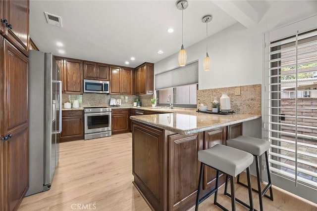 kitchen with tasteful backsplash, stainless steel appliances, a peninsula, light wood-type flooring, and visible vents
