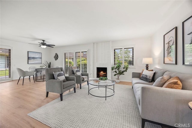 living room featuring ceiling fan, a fireplace, and light wood-style flooring