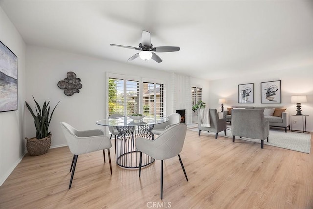 dining room with baseboards, a ceiling fan, light wood finished floors, and a brick fireplace