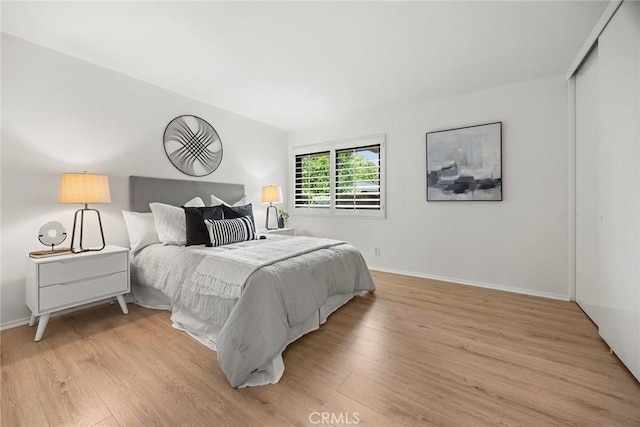 bedroom with light wood-style floors, baseboards, and a closet
