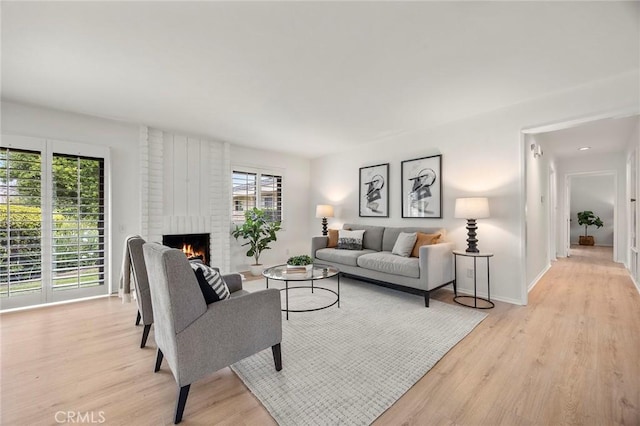 living room with light wood-type flooring, baseboards, a brick fireplace, and a healthy amount of sunlight