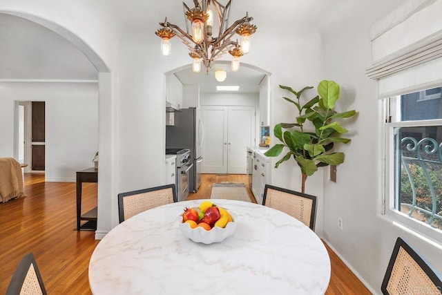 dining area with arched walkways, a chandelier, plenty of natural light, and light wood-style flooring