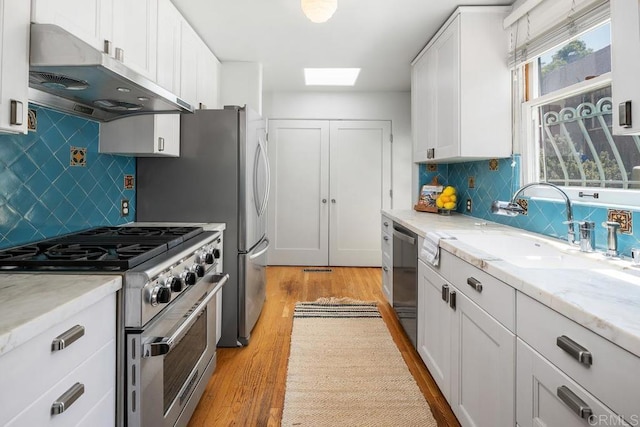 kitchen with light wood-style floors, under cabinet range hood, white cabinets, a sink, and stainless steel appliances
