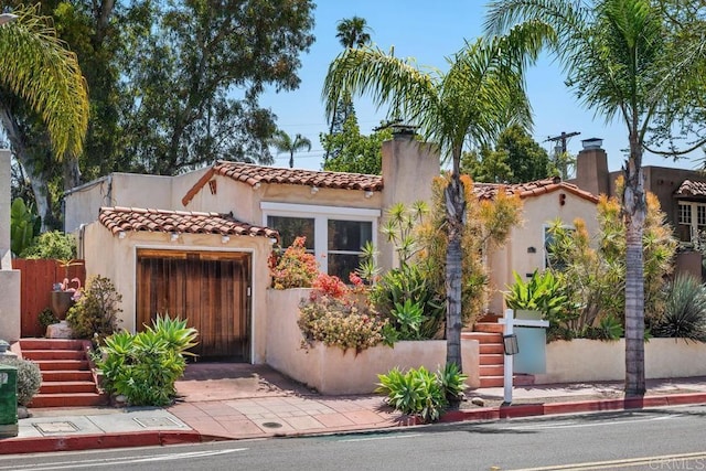 mediterranean / spanish house featuring a chimney, an attached garage, a tile roof, and stucco siding