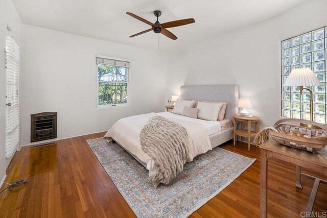 bedroom with ceiling fan, heating unit, and wood finished floors
