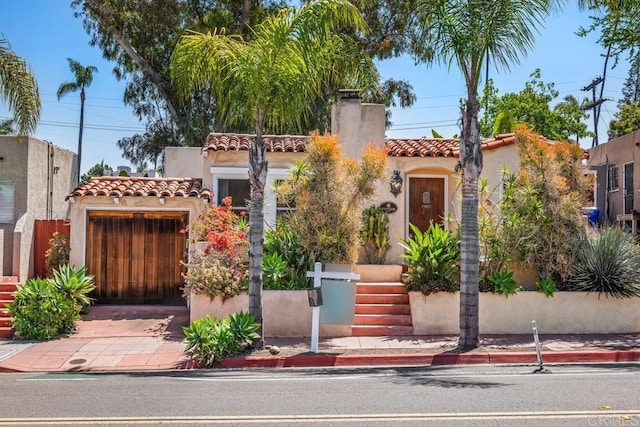 mediterranean / spanish-style home with stucco siding, a chimney, a tiled roof, an attached garage, and driveway