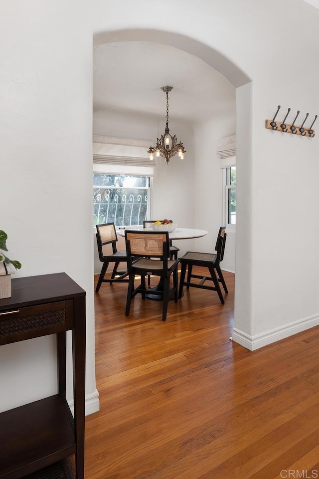 dining space featuring an inviting chandelier, arched walkways, wood finished floors, and a healthy amount of sunlight