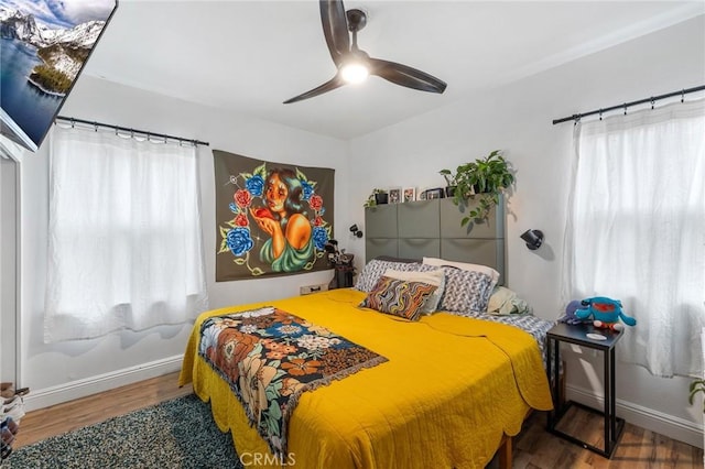 bedroom with baseboards, a ceiling fan, wood finished floors, and multiple windows