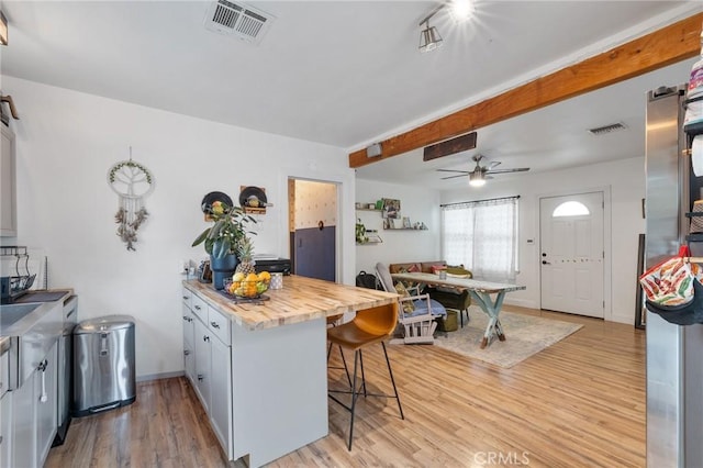 kitchen with ceiling fan, a kitchen bar, light wood-style flooring, and visible vents