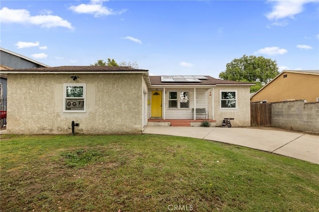 rear view of house with a lawn, fence, roof mounted solar panels, and stucco siding