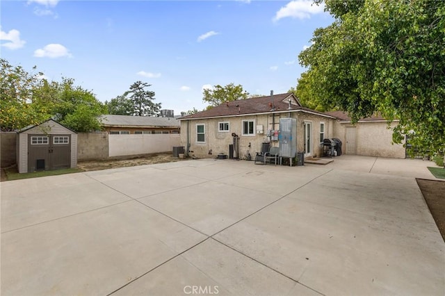 back of property with an outdoor structure, cooling unit, a fenced backyard, a shed, and a patio area