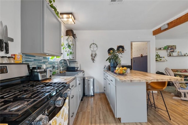 kitchen with a sink, stainless steel range with gas stovetop, a kitchen breakfast bar, a peninsula, and backsplash