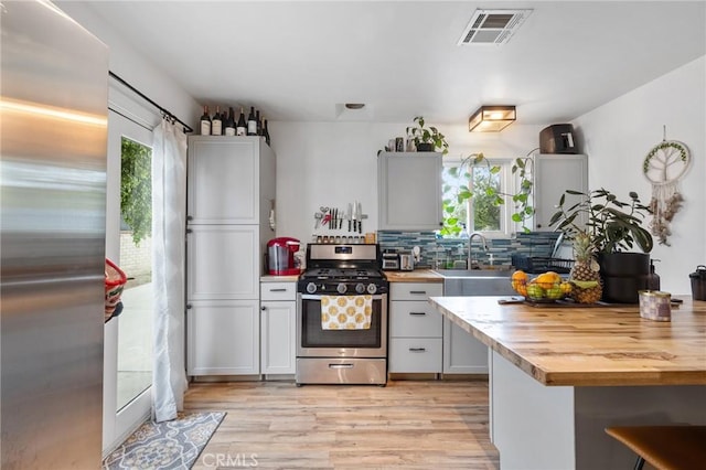 kitchen featuring visible vents, a sink, stainless steel gas range oven, and wooden counters