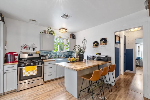 kitchen with visible vents, gas stove, a sink, wood counters, and a breakfast bar