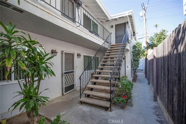 view of exterior entry with visible vents, fence, and stucco siding