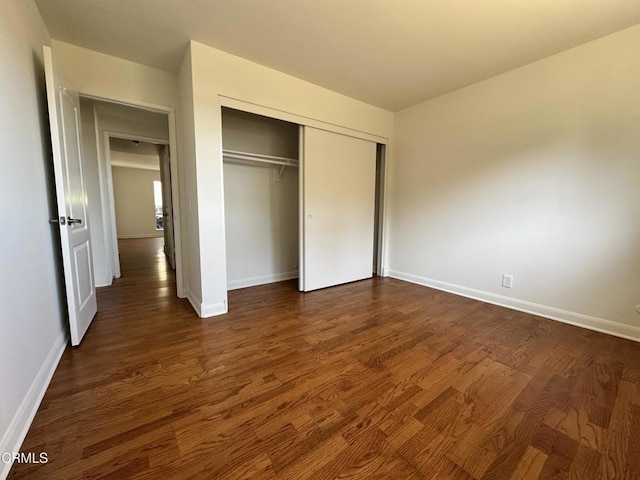 unfurnished bedroom with dark wood-style flooring, baseboards, and a closet