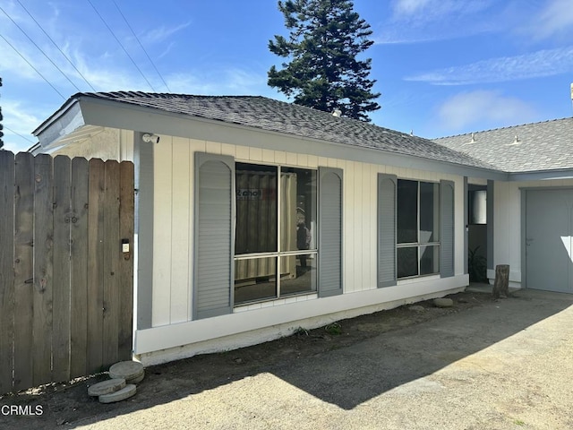 view of home's exterior featuring fence, roof with shingles, and a garage