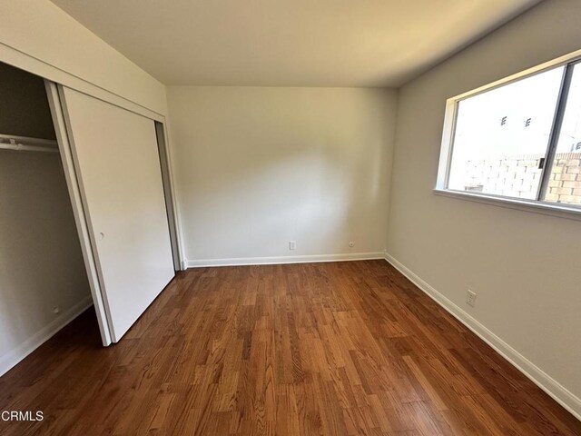 unfurnished bedroom with baseboards, a closet, wood finished floors, and multiple windows