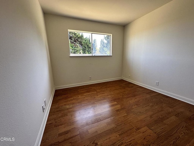 unfurnished room featuring baseboards and dark wood-style floors