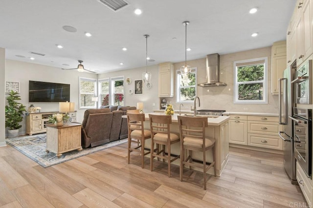 kitchen featuring light wood-style flooring, visible vents, open floor plan, wall chimney exhaust hood, and a kitchen island with sink