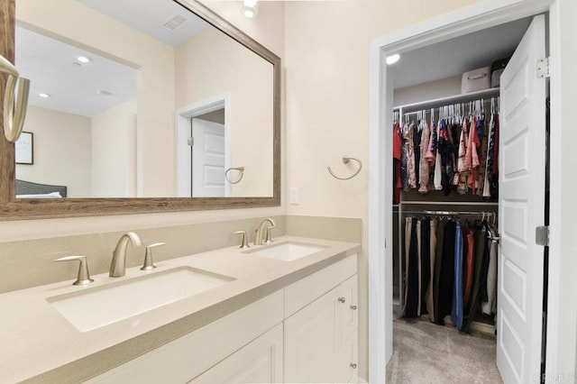 full bathroom featuring visible vents, double vanity, a sink, and a walk in closet