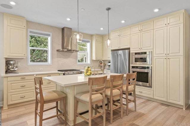 kitchen featuring appliances with stainless steel finishes, light wood-style flooring, a wealth of natural light, and wall chimney exhaust hood