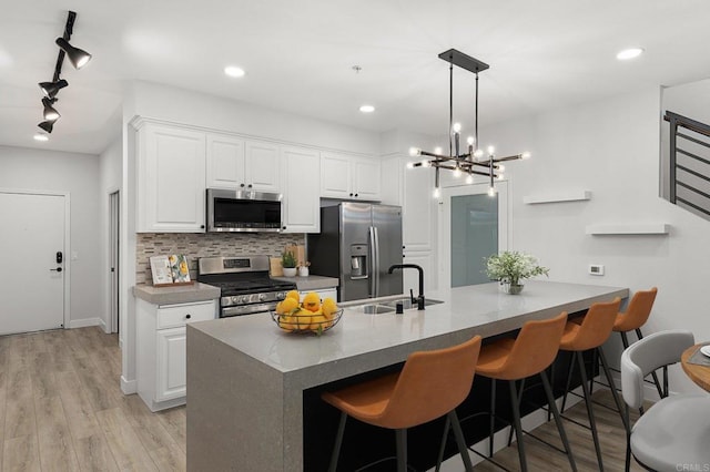 kitchen featuring track lighting, decorative backsplash, white cabinetry, a sink, and appliances with stainless steel finishes