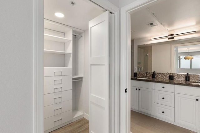 full bath with a sink, visible vents, double vanity, and wood finished floors