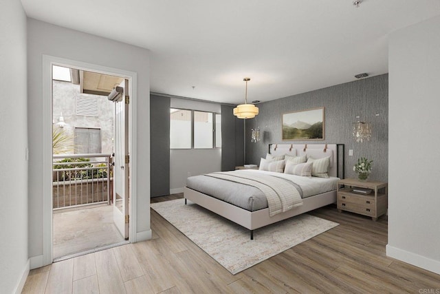 bedroom featuring baseboards, wallpapered walls, wood finished floors, and an accent wall